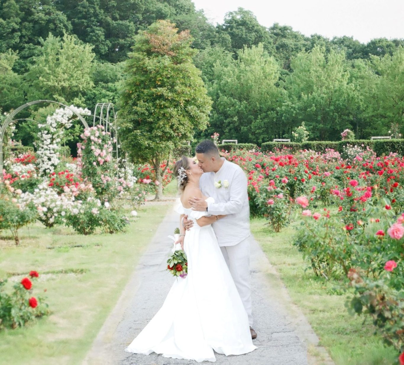 Wedding Couple in Garden Bride and groom embrace in a rose garden, surrounded by lush greenery.